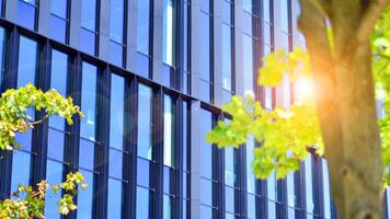 City life, urban landscape and ecology. Modern office complex with glass facades and smooth lines against backdrop of green trees, concept of modern architecture. Organically building into nature. photo