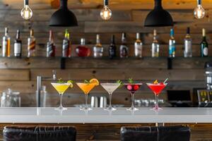 A row of five colorful cocktails sit on the bar counter ready to be served to patrons photo