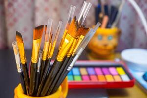 Artistic equipment. Painting brushes with a watercolor color palette background. Paint brushes, watercolor color palette on work table. A set of brushes photo