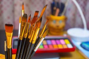 Artistic equipment. Painting brushes with a watercolor color palette background. Paint brushes, watercolor color palette on work table. A set of brushes photo