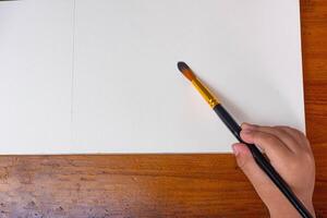Child painting in blank drawing book with brush and watercolor color palette. Paint and watercolor accessories and Blank Books on Wooden Table. Flat lay, top view. Place for text photo