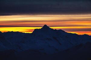 Sharp mountain peaks, silhouette of snow-capped mountains against the backdrop of a beautiful colorful sunset and clouds photo