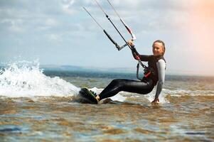Smiling woman with a kiteboard looks at the camera while sailing through the waves on a parachute, kite. Fast travel with a wave from the board photo
