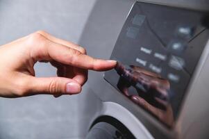 close up view of a washing machine set to low temperature wash cyle to reduce cost and energy to clean laundry, persons hand shown about to press the start button photo