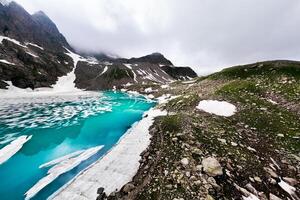 Tranquil landscape with snow lake in clouds. Mountain stream flows into glacial lake. Snowy mountains in beginning fog. Alpine lake photo