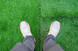 Cropped shot view of someone standing on green artificial turf in garden. Artificial grass are made by polyethylene or nylon, convenient and it does not require much maintenance. photo