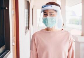 Asian woman wearing mask and face shield before going outside her room for prevent and protection covid-19 virus disease. Conceptual of new normal lifestyle after Covid-19 pandemic outbreak. photo
