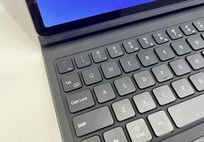 Tablet attached to gray colored keyboard. Modern gadget isolated on horizontal white desk surface background. photo