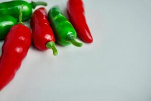 Plastic toy green and red chilli hot pepper food ingredients isolated on horizontal empty copy spaced white surface background. photo