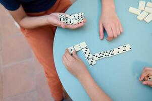 Close-up of children playing a game of dominoes on a blue table, focusing on strategic hand placement and number matching photo