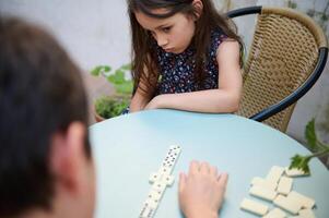 Thoughtful young girl playing a game of dominoes with a friend, captured in a moment of concentration at the table. photo