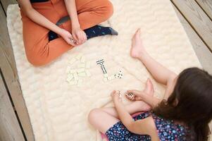 Children playing a fun game of dominoes on a soft beige blanket, enjoying a cozy indoor afternoon, connecting over a classic board game in a warm and comfortable setting photo