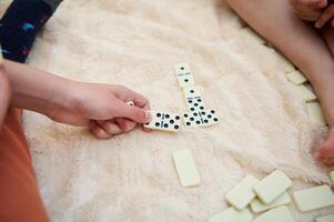 People playing dominoes on a soft blanket, focusing on hands and gameplay pieces, capturing a cozy and engaging pastime activity with a warm, relaxed atmosphere. photo