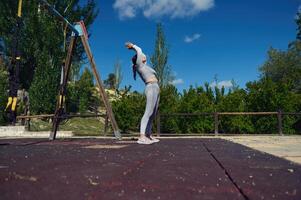 Woman stretching outdoors at a sunny fitness park, reaching towards the sky in a serene exercise routine. Capturing tranquility and focus in a natural environment for a healthy lifestyle. photo