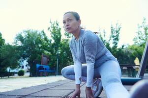 Woman in athletic attire warming up with a stretch outdoors on a sunny day, demonstrating focus, strength, and dedication to fitness in a green park setting photo