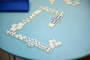 Dominoes game in progress on a round blue table, showcasing a strategic layout with pieces interconnected and box nearby, evoking a sense of leisure and strategy. photo