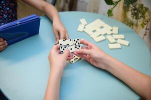 Children playing a game of dominoes at a round blue table, focusing on strategy and fun in a relaxed setting with friends. photo