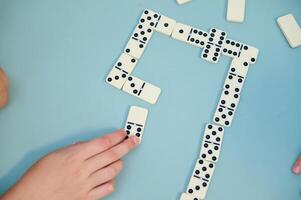 Hands playing a strategic game of dominos on a light blue table surface with scattered tiles and focused players. photo