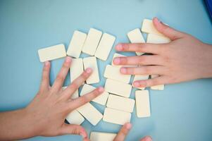 Children playing with white domino tiles on a blue table, showcasing teamwork and strategy in a fun and engaging way through hands-on learning and development. photo