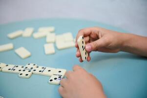 Hands engaging in a strategic game of dominoes on a light blue surface, focusing on the tactile interaction and concentration involved in gameplay. photo