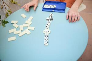 Close-up of a tabletop domino game in progress, featuring hands and scattered tiles on a blue surface in a relaxed setting photo