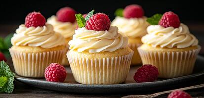 A plate of cupcakes with raspberries on top. The cupcakes are frosted and have a light, fluffy texture. The raspberries are fresh and add a pop of color to the cupcakes photo