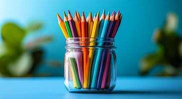 A jar full of colorful pencils on a blue table. The jar is full of pencils of different colors, and the pencils are arranged in a way that they are all visible. Concept of creativity and organization photo