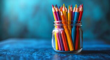 A jar full of colored pencils on a blue table. The pencils are in different colors and are arranged in a way that they are all visible photo