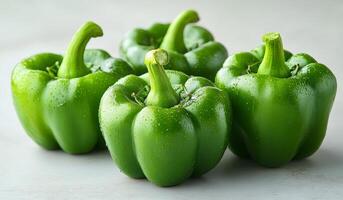 Four green peppers are sitting on a counter. They are fresh and ready to be eaten. The peppers are arranged in a row, with one on the left, one in the middle, and two on the right photo
