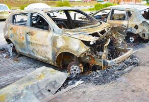 A back view of a blown up down car. A charred burned down vehicle in the city center in residential area. Absolutely destroy sedan car in the parking lot after the bombing by cluster bomb photo