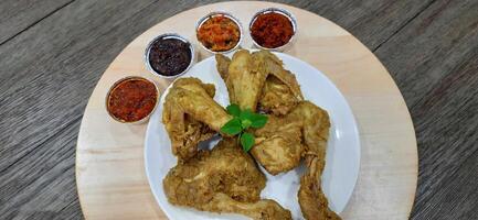 Ayam ungkep bumbu kuning or boiled chicken with curry seasoning and coconut water. Served with varian sambal or hot chili sauce. Ready to fried photo