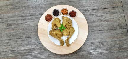 Ayam ungkep bumbu kuning or boiled chicken with curry seasoning and coconut water. Served with varian sambal or hot chili sauce. Ready to fried photo
