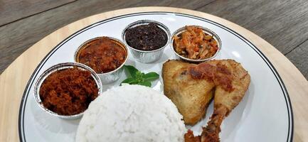 Ayam ungkep bumbu kuning or boiled chicken with curry seasoning and coconut water. Served with varian sambal or hot chili sauce. Ready to fried photo