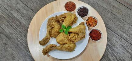 Ayam ungkep bumbu kuning or boiled chicken with curry seasoning and coconut water. Served with varian sambal or hot chili sauce. Ready to fried photo