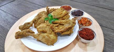 Ayam ungkep bumbu kuning or boiled chicken with curry seasoning and coconut water. Served with varian sambal or hot chili sauce. Ready to fried photo