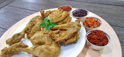 Ayam ungkep bumbu kuning or boiled chicken with curry seasoning and coconut water. Served with varian sambal or hot chili sauce. Ready to fried photo