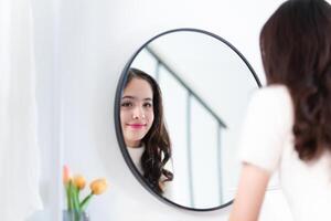 Smiling of cheerful beautiful pretty teenage girl felling relaxing and enjoy time look at mirror in home, Young girl applying makeup photo