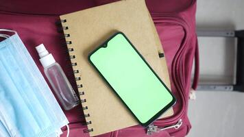 A green notebook, a phone, a mask and a bottle of hand sanitizer on a video