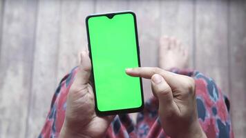 A man is using a smartphone with a green screen and a person is sitting on the floor video