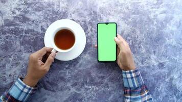 Top view of hands holding smartphone and cup of tea on concrete background video