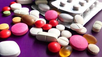 Many different types of pills and tablets are scattered on a purple surface video