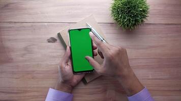 A man is using a smartphone with a green screen on a wooden table video