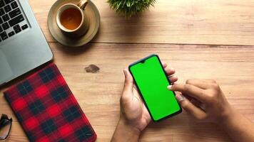 A person using a smartphone with a green screen on a wooden table video