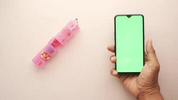 A hand holding a smartphone with a green screen and a pill box on a white background video