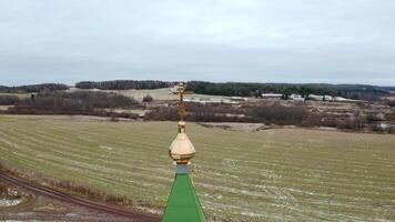 Initial winter. Clip.View from a drone on a landscape with snowy grass in a field where there is a temple with a golden cross on a golden dome against the blue sky. video