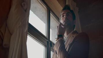 Low angle view of a man in brown suit standing by the window. Action. Thoughtful man inside the room. video