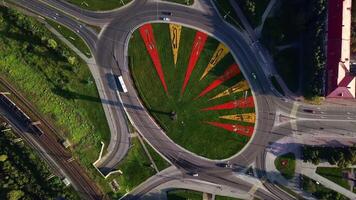 Aerial view of a round shaped crossroad with moving cars. Clip. Green meadow and bright growing flowers creating triangular pattern. video