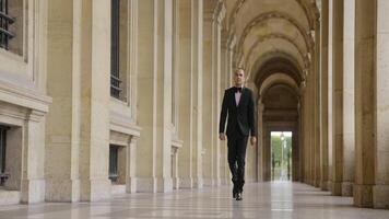 Man in black and white official suit walking in arcuate shaped hall. Action. Man walking outdoors by the building with columns. video