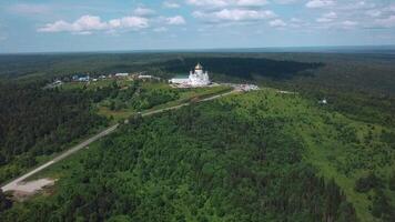 View from a height of a summer landscape with a forest and mountains. Clip. A green forest with spruces and a beautiful peasant temple in the middle surrounded by a village. video