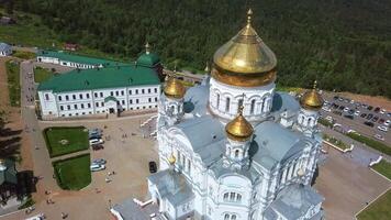 Aerial view on great white christian church with golden domes on the hill and field with forest background. Clip. Concept of religion. video